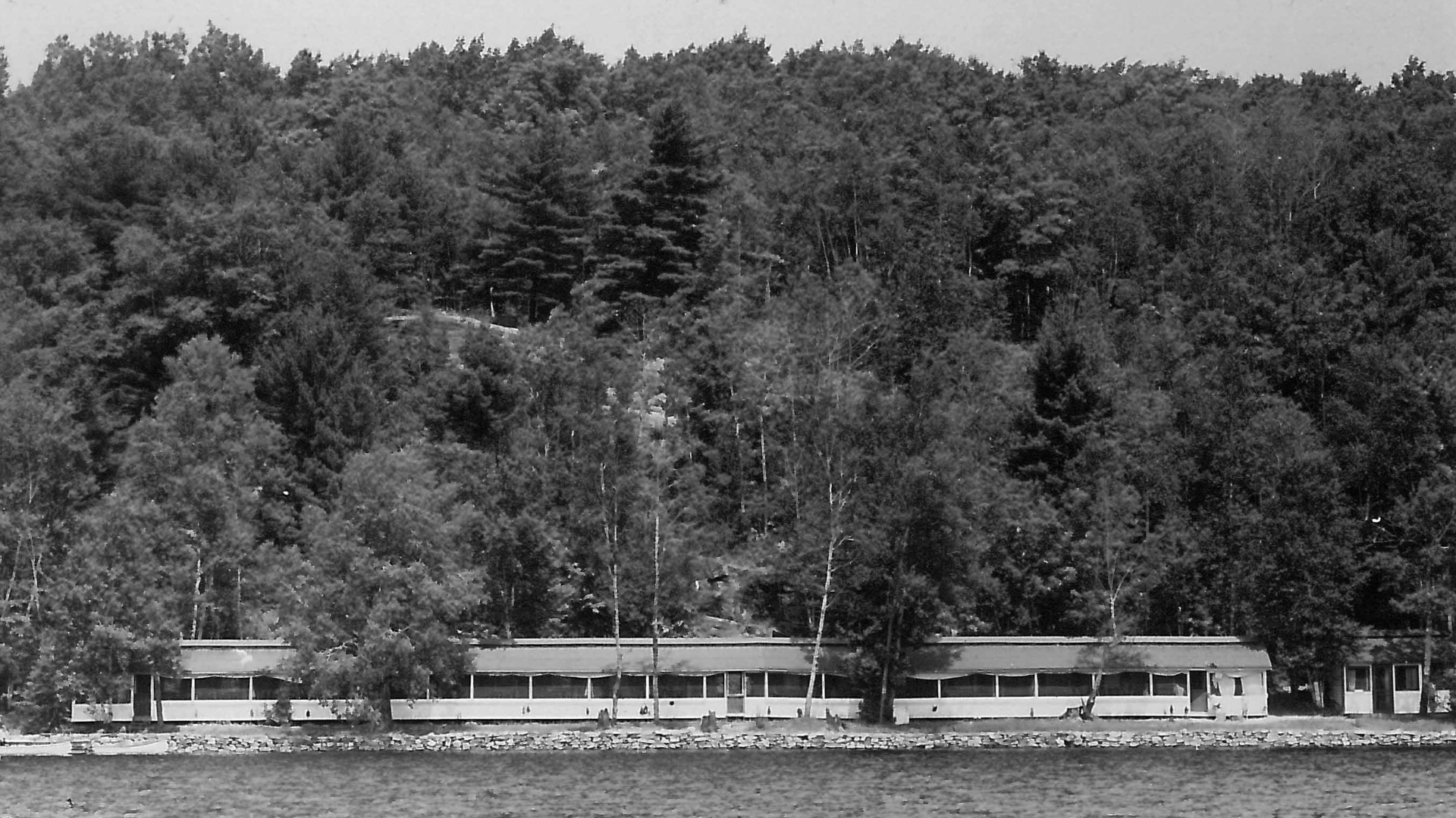 Black and white photo of a long building by the lake.