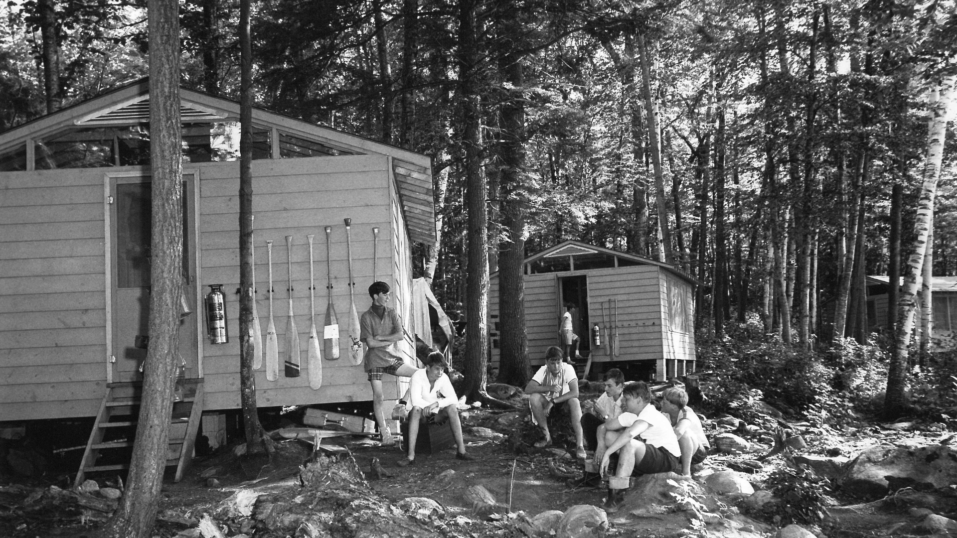Black and white photo of campers sitting outside a cabin.