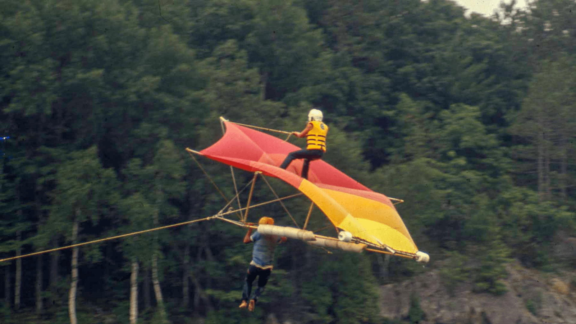 A person hang gliding over a lush green forest landscape.