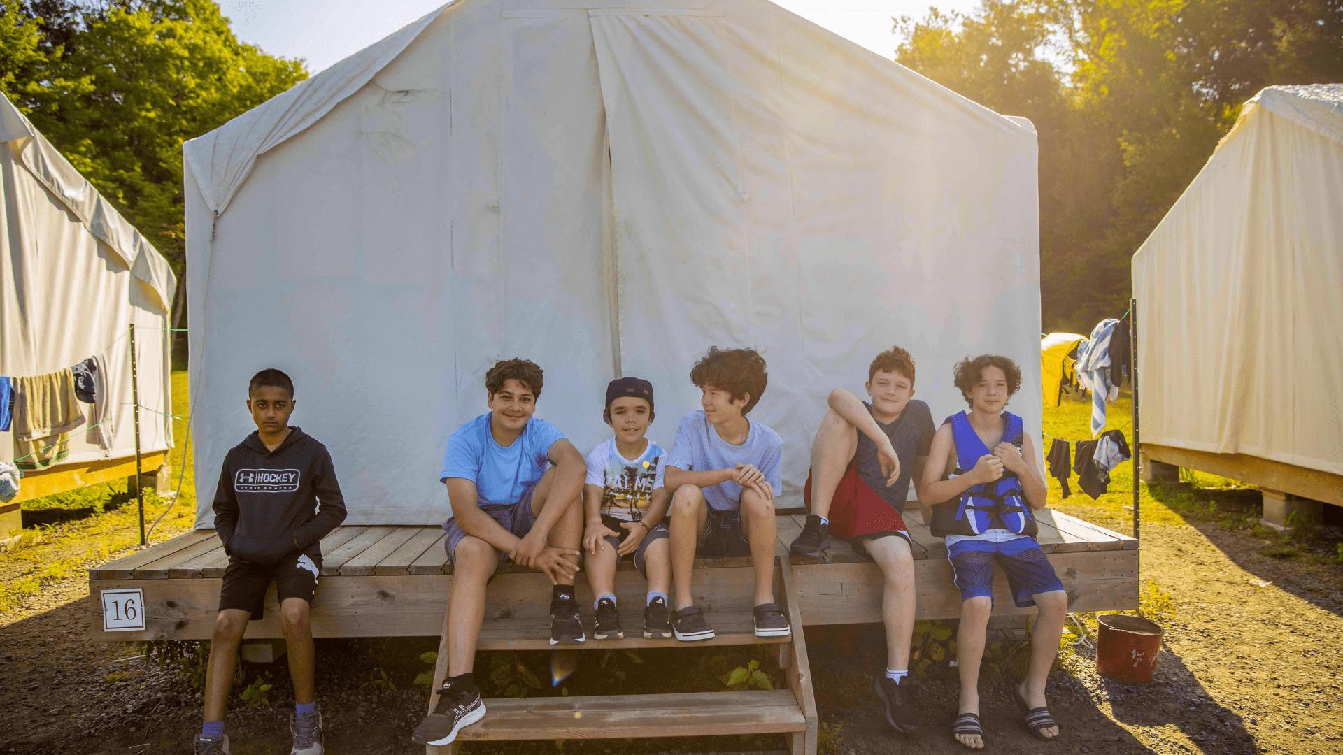 Five young boys sitting on stairs outside a white tent.